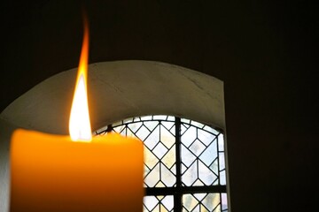 Gelbe Kerze mit Flamme vor Gitterfenster mit Rundbogenmuster in Klosterkirche 