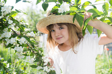 little girl in a straw hat holding and inhaling jasmine scent amid flowering jasmine bushes in garden in summer. Aromatherapy and Spa concept.natural eco product. stress relief