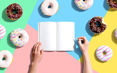 Person writing in a notebook with a collection of donuts - 751416383
