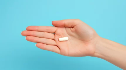 Fotobehang A hand holding two white capsules against a blue background. Ai generative illustration © ImageFlow