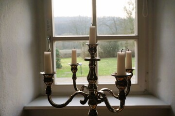 Innenausstattung mit silbernem Kerzenleuchter und weißen Kerzen altem Fenster mit weißem Rahmen...