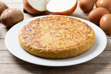 Traditional spanish omelette with ingredients on wooden table.