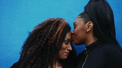African American adolescent daughter kissing mother in the forehead showing family love and...