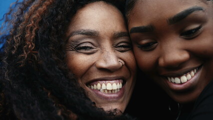Happy African American mother and daughter's close-up faces in cheek to cheek portrait embrace,...