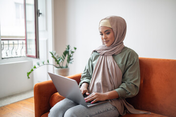 woman in headscarf works on her laptop sitting at home