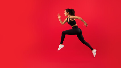 Fit woman in sportswear leaps energetically against vibrant red background