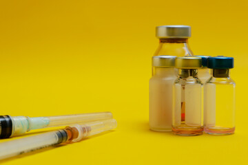 photo of several vials of injection medicine and syringes isolated on a yellow background