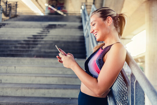 Beautiful sports woman resting after training outdoors. Smiling woman using the phone.