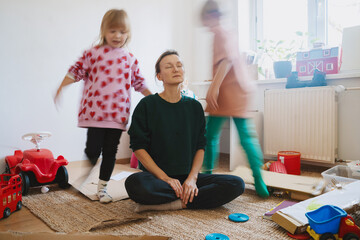 Stressed out mother sitting on floor while children running around her.
