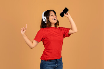 Happy young arabic woman singing karaoke on beige background