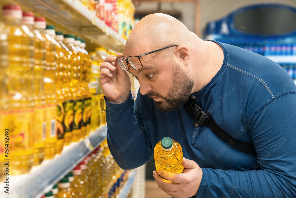 Wall mural shocked overweight man raising his glasses to his forehead and looking on price of vegetable oil in  - Wall murals
