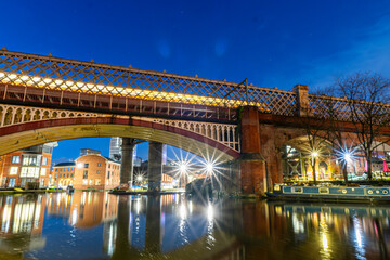 Long exposure night photo of a bridge and a tram driving over it at Castlefield, Manchester. 