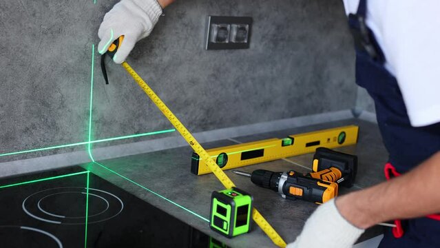 Man in uniform measures the level of the countertop with ruler and laser when assembling furniture.