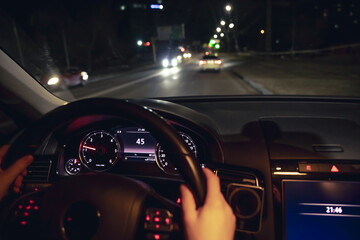 Driver's hands on the steering wheel of a car at night, night driving.