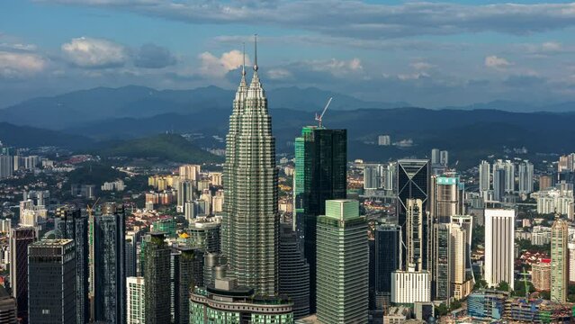 breathtaking aerial perspective of Kuala Lumpur's cityscape, prominently featuring the Petronas Twin Towers surrounded by high-rise buildings against a backdrop of distant mountains and clouds