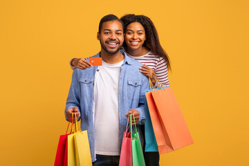 Joyful young black couple showing credit card and holding colorful shopping bags