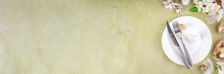 Easter table setting with spring flora, plate, knife and fork with Easter eggs and nests on background. Easter light green cutlery flat lay for festive greeting card, menu, invitation, copy space 