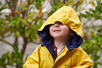 Child, rain and raincoat outdoor in winter for fashion, jacket and cold weather in London. Little boy, male toddler and kid in drizzle by tree, bokeh or environment with windbreaker for chilly season © peopleimages.com