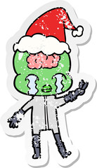 distressed sticker cartoon of a big brain alien crying and giving peace sign wearing santa hat