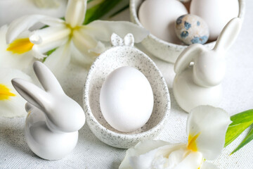 Closeup one white egg in marble bowl with bunny ears, small bunnies, Iris flowers around it on white