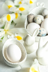 Easter eggs in marble bowls with bunny ears, small ceramic bunnies, white Iris flowers on white.