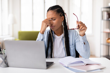 Stressed black lady student with headache studying at laptop