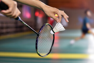 Badminton player holds racket and white cream shuttlecock in front of the net before serving it to...