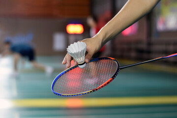 Badminton player holds racket and white cream shuttlecock in front of the net before serving it to...
