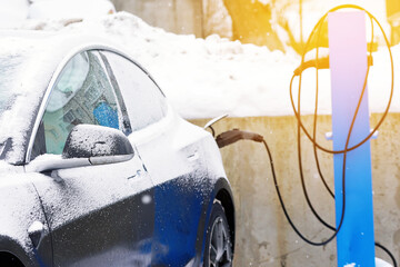 Electric car parked at charging station and charge battery in snowy day. Electric vehicle...