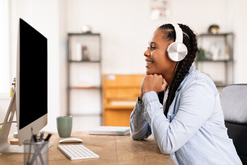 Happy black lady student in headphones enjoying online lesson on her computer