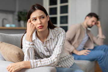 Upset young couple with problems sitting apart on sofa
