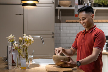 Handsome and happy young man preparing food, mixing ingredients on a wooden bowl in the kitchen