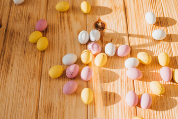 Multi-colored chocolate decorative eggs on a wooden background with sun reflections. Happy Easter background. Top view