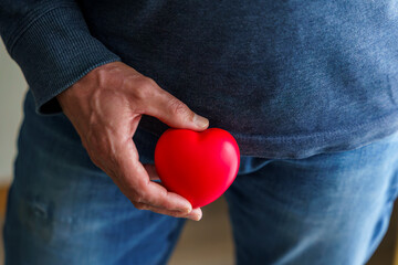 Ein Mann hält ein rotes Herz an seinen Unterlaib. Krebsvorsorge. 