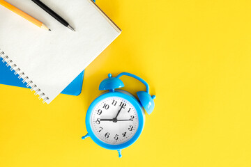Blue alarm clock and notepads on a yellow background, flat design.