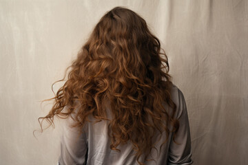 Back view young woman with auburn hair on a light gray background. - obrazy, fototapety, plakaty