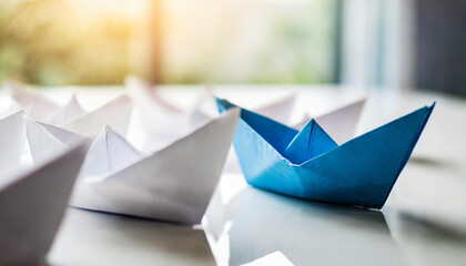 blue paper ship leads a fleet of white paper ships on a modern white table, symbolizing leadership and teamwork - obrazy, fototapety, plakaty