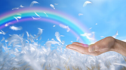 Sending beautiful rainbow healing energy out - male hand with rainbow arcing from his palm against  blue sky and fluffy white feathers floating in the sky and below with space for a spiritual message - 751522937