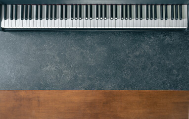 Piano keyboard on a dark marble and wood surface, top view.