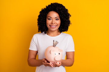 Fototapeta na wymiar Photo of positive cheerful intelligent woman dressed white t-shirt hold piggy money box in hands isolated on yellow color background