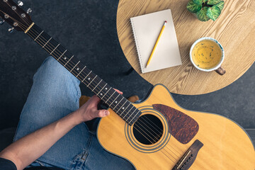 A man with an acoustic guitar and a notepad with a cup on the table, top view.
