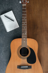 Obraz premium Acoustic guitar and notebook on a textured black and wooden background.