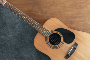 Acoustic guitar on a textured black and wooden background, top view.