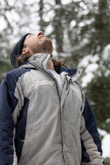 A man wearing a gray and blue jacket is standing in the snow. He is looking up at the sky