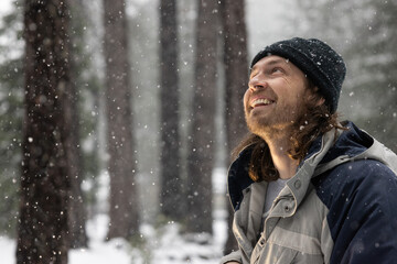 A man wearing a black hat and a blue jacket is smiling as he looks up at the snow falling from the sky