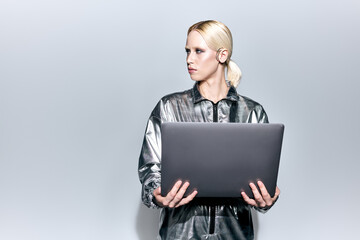 extravagant beautiful woman in silver robotic clothing posing in motion with laptop and looking away