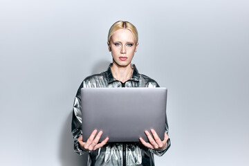 beautiful blonde female model in robotic silver outfit holding laptop and looking at camera