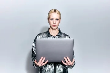 Zelfklevend Fotobehang beautiful blonde female model in robotic silver outfit holding laptop and looking at camera © LIGHTFIELD STUDIOS