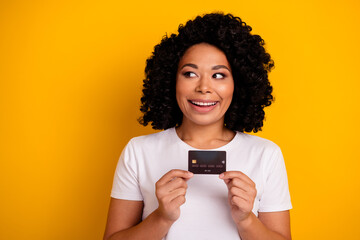 Portrait of optimistic girl with perming coiffure demonstrate debit card look at offer empty space isolated on yellow color background