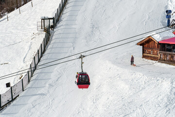 Serene snowy landscape with a red cable car, a woman with a sleigh and a cozy hut, representing the...